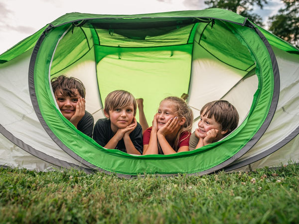 Four children smiling while hanging out in a tent outdoors
