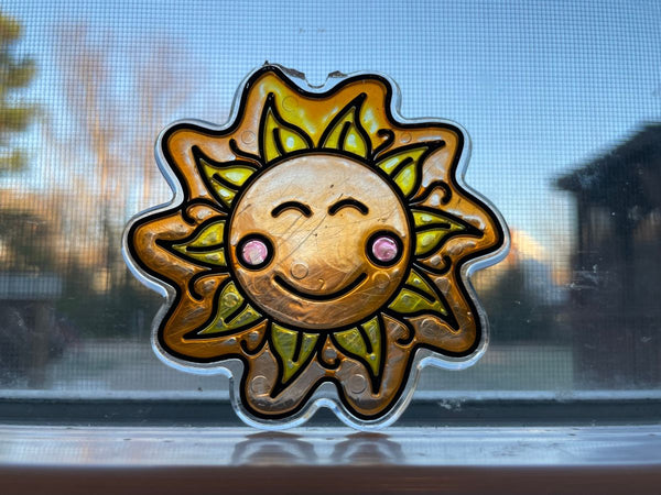 A sun shaped sun catcher leaning on a window overlooking a sunny backyard