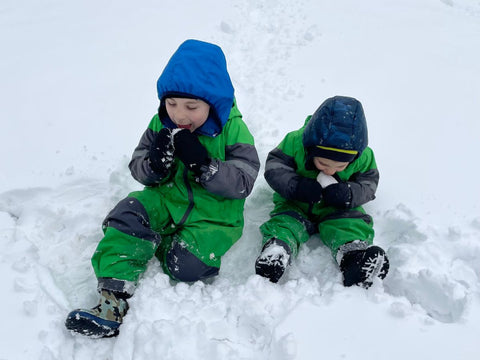 Two young boys laying in the snow wearing Oakiwear Rain Suits