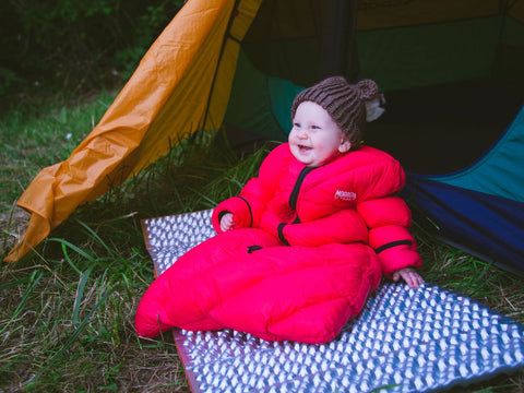 A baby wearing a red Morrison Outdoors Little Mo Sleeping bag in front of a tent