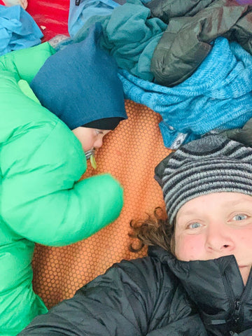 A woman laying on a camping mattress next to a toddler wearing a Morrison Outdoors Big Mo sleeping bag