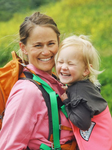 Woman with a smiling in a Trail Magik child carrier attached to her hiking backpack