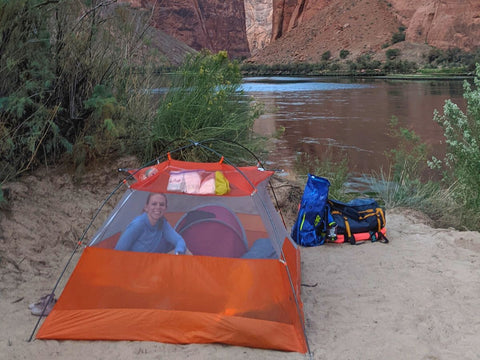 A woman smiling inside a tent along the banks of a river within Glen Canyon