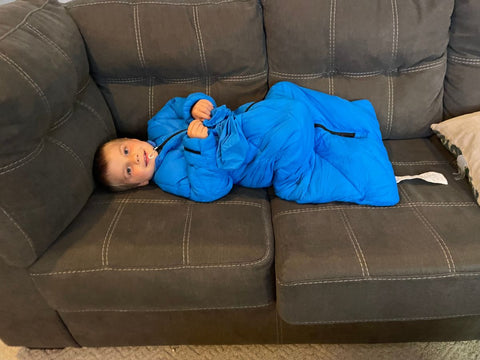 A young boy laying on a couch wearing a blue Morrison Outdoors sleeping bag