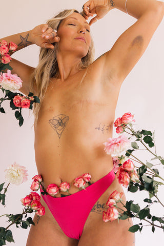 Close up photo of Holly wearing a Huha High Rise Thong wearing Awareness Pink surrounded by roses and pink flowers.