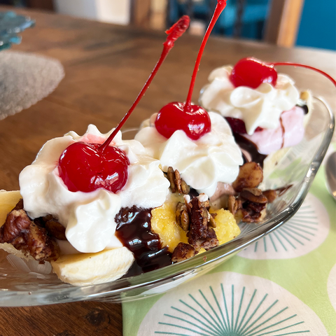 A low-carbish Better Than Banana Split made with Better Than Provisions Better Than Granola on a slim glass boat, placed over a lime green tablecloth