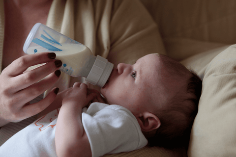 Adult hand holding bottle and baby drinking out of bottle