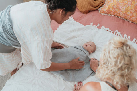 Swaddling baby, two women peering over baby to correctly swaddle baby