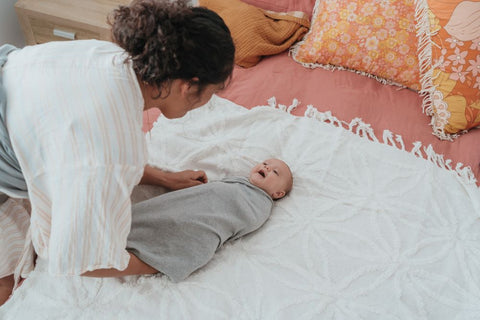 Baby laying on bed swaddled by BlankyDink, BabyDink's Swaddle. Mother smiling