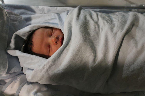 The image above showcases an example of an incorrectly swaddled newborn. Notice that the swaddle is too close to the baby's mouth and covers its head, which are both practices to avoid