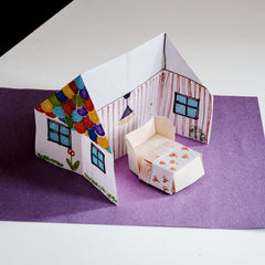 An origami house, decorated with color felt tip pens, and featuring an origami bed in a photo for NiMi Projects origami workshops.