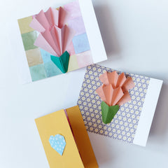 Three cards with popup two tiered flowers in pink and orange on patterned backgrounds in a photo for NiMi Projects origami workshops.