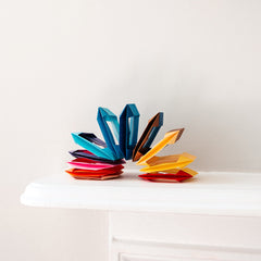 A rainbow coloured origami slinky, opened up and displayed on a white shelf in a photo taken by NiMi Projects for its origami workshops.