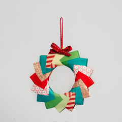 A multicolored and multi-patterned origami wreath, topped with a red ribbon in a photo for NiMi Projects workshops.