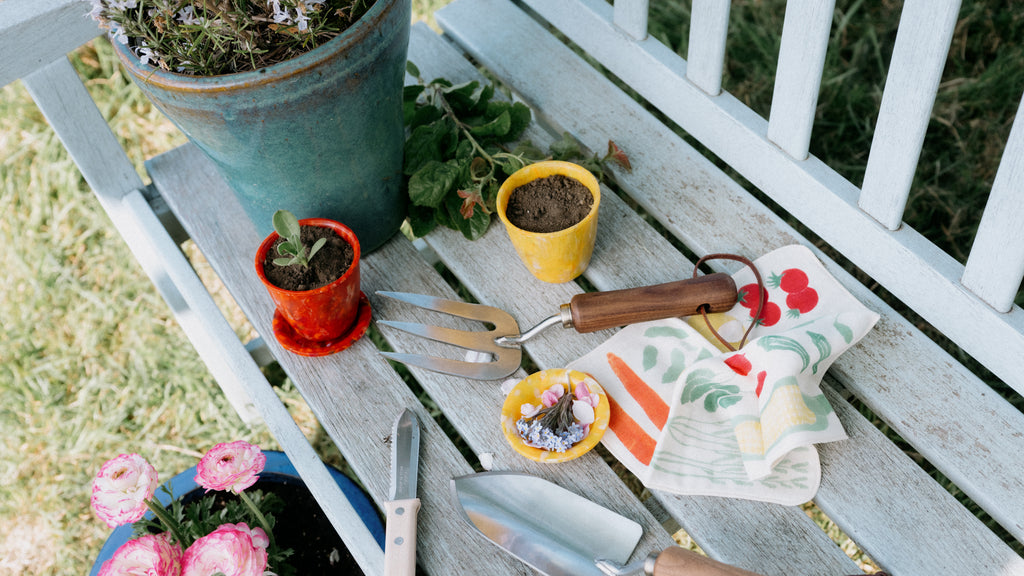 A display of Asano Mokkousho’s stainless steel fork and trowel with wooden handles, and a hori hori mini trowel with beech wood handle, displayed with a red Buoy recycled plastic plant pot. Available at NiMi Projects UK.