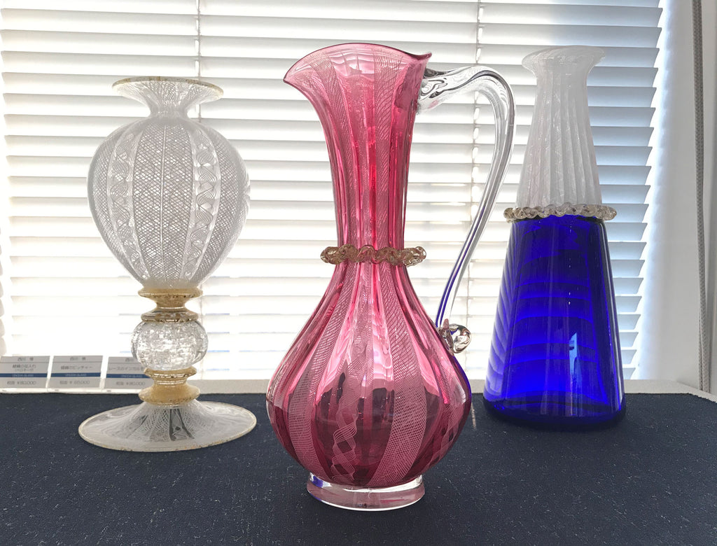 Three Japanese glass artisans glass vessels, a vase with white lace-like patterning, a pink jug and a blue vase, on show in Toyama, Japan.