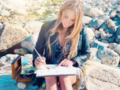 portrait of tarot deck artist, lisa santine, working on the artwork for the deck while sitting at the beach.