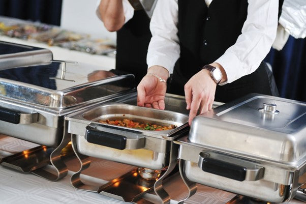 A group of servers places food on the chafers.