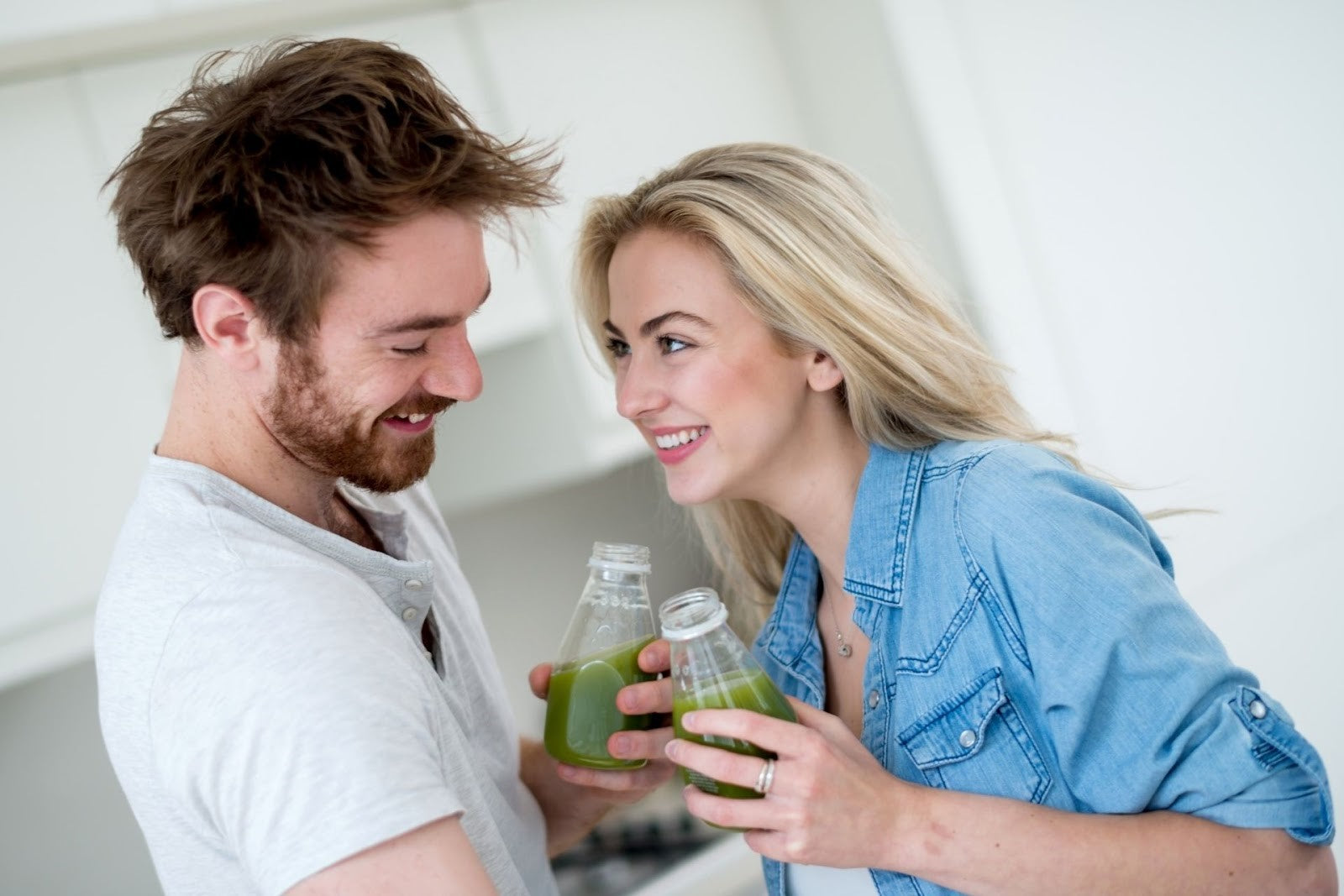 A man and a woman smiling at each other while holding bottles of green juice