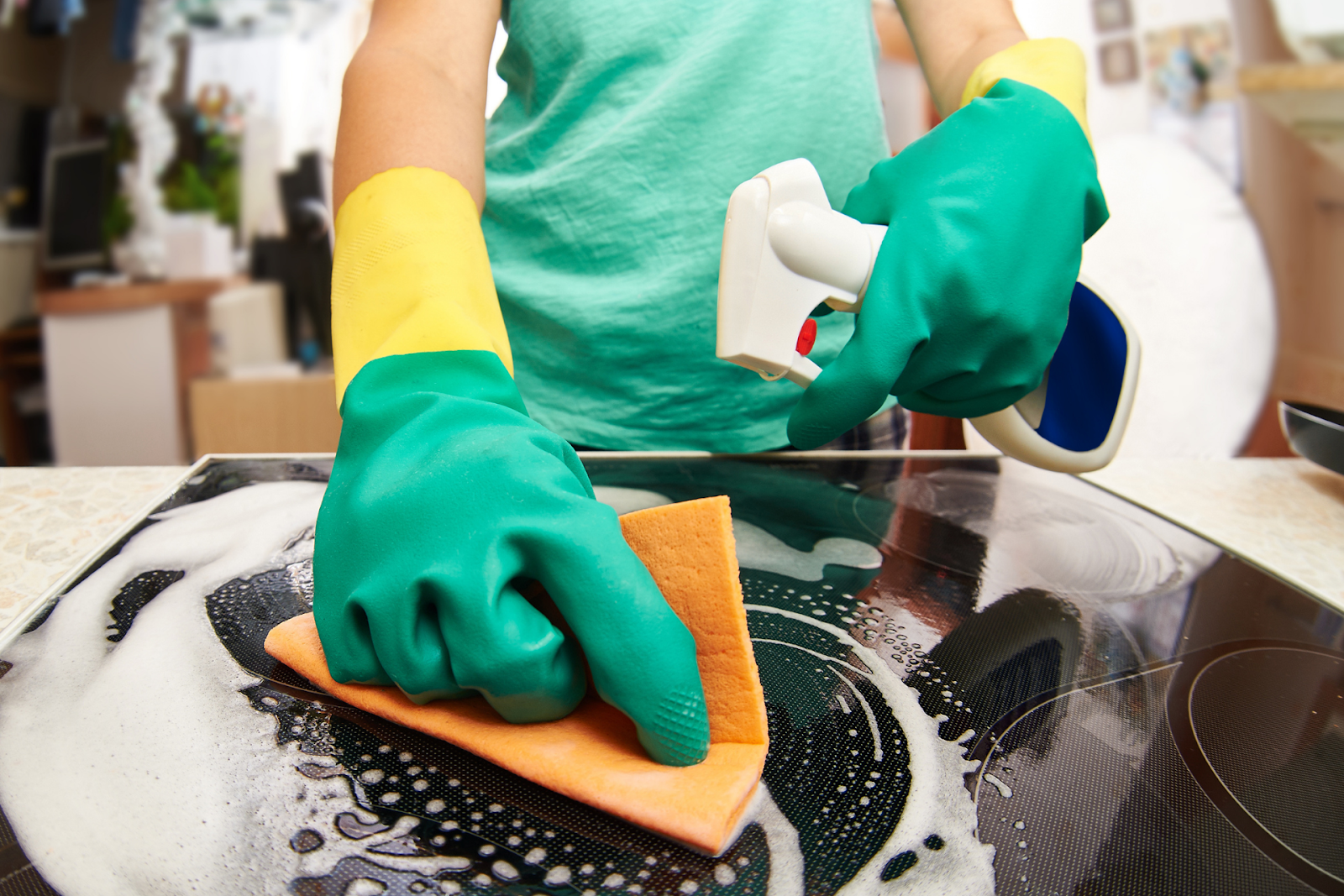 A person wearing rubber gloves spraying an electric stove with disinfectant