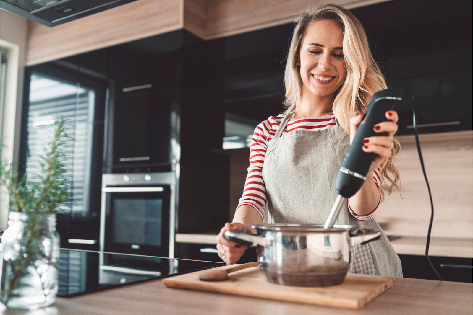 A woman using an immersion blender to blend soup