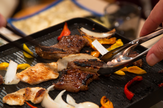 A closeup of someone grilling meat and veggies on a smokeless indoor BBQ grill