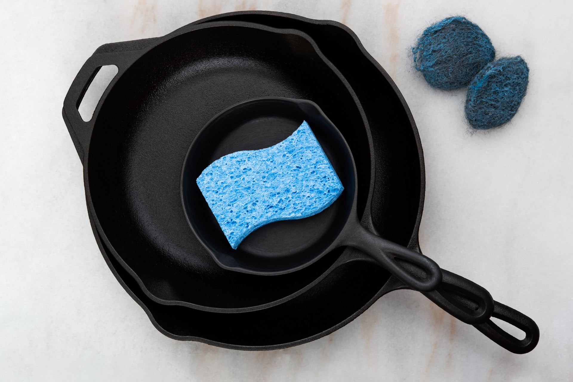 three stacked cast iron pans with a blue sponge sitting on top