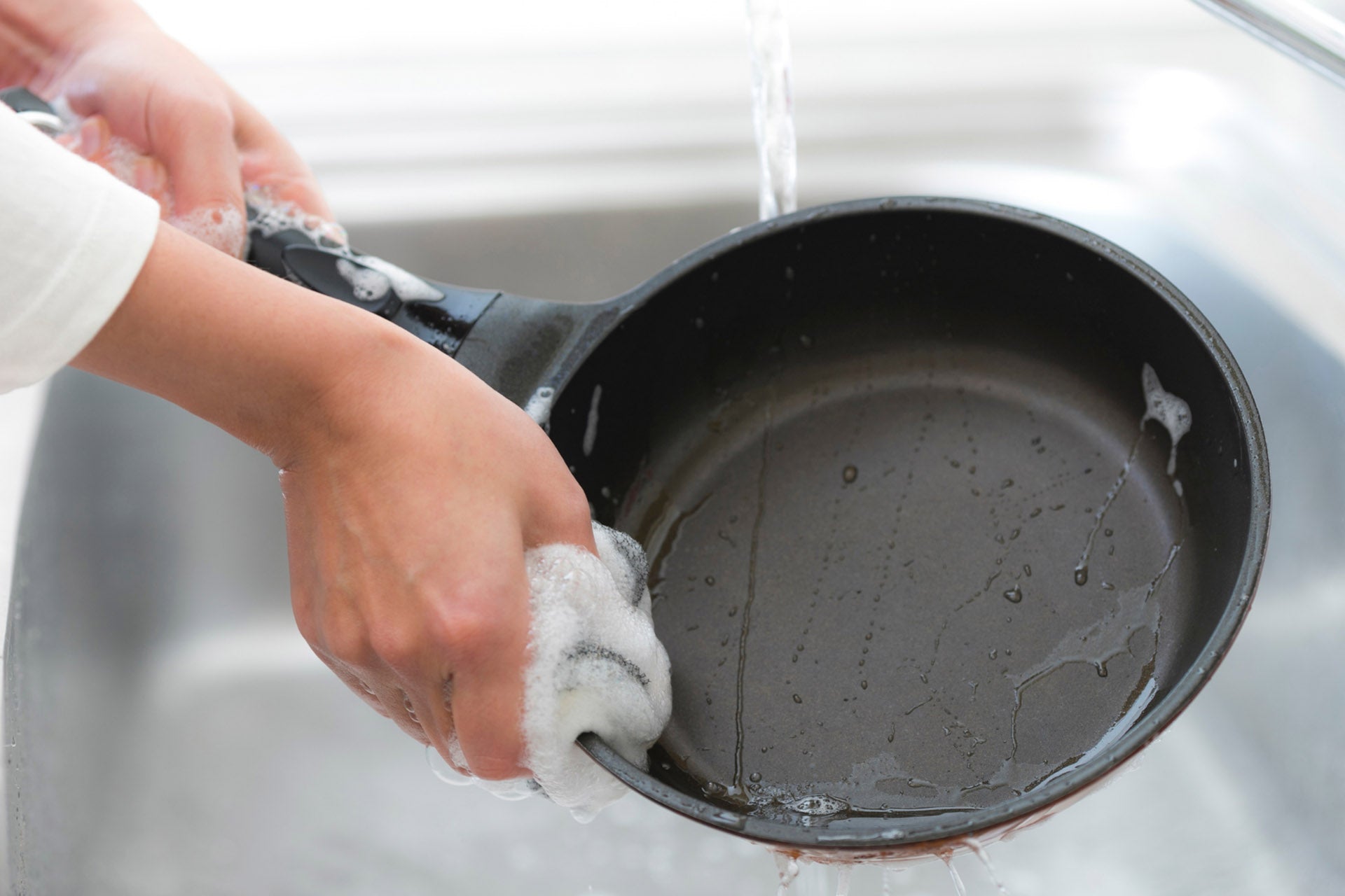 A cast iron pan being washed with soap in a sink