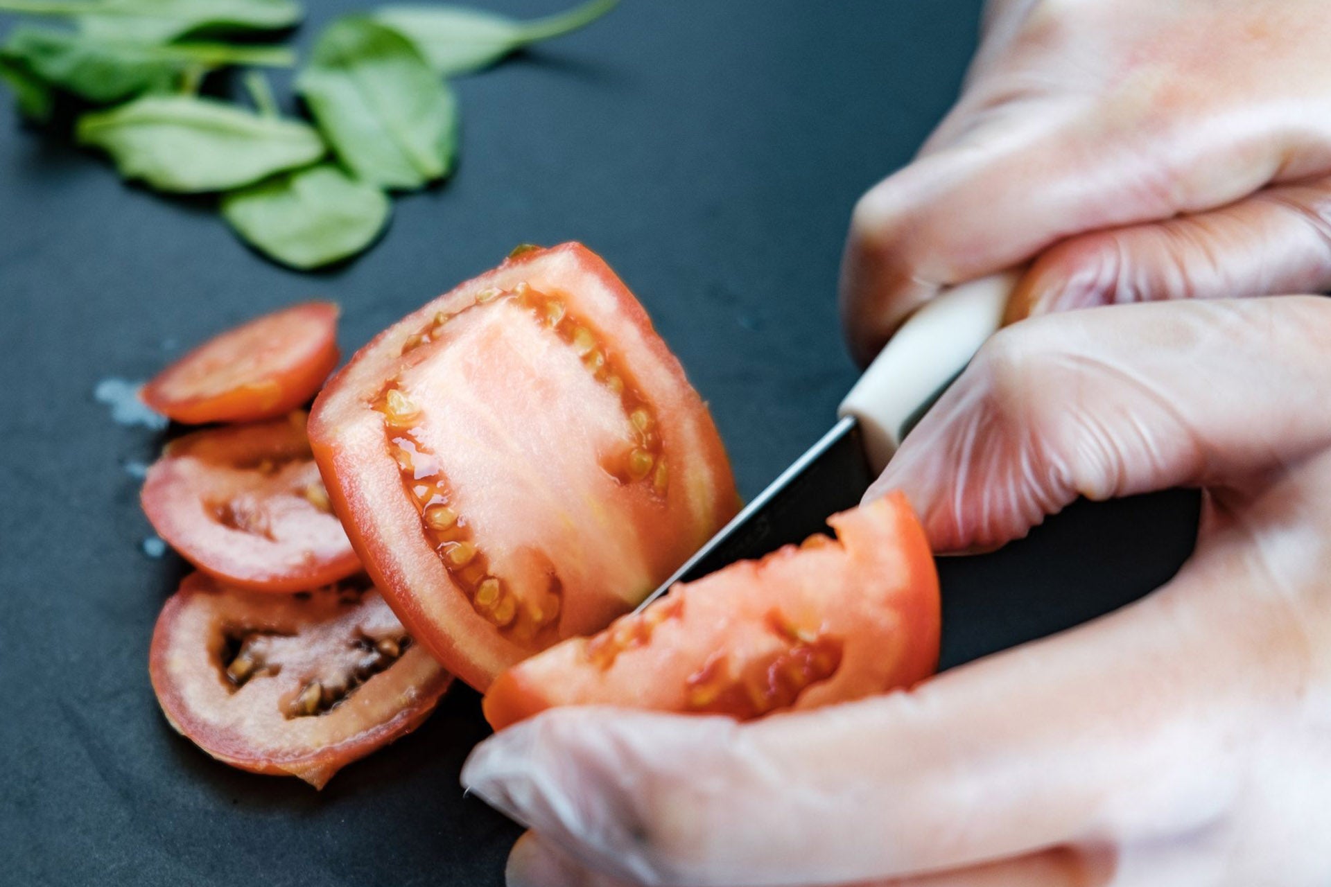 A person wearing food-grade vinyl gloves while slicing tomatoes on a chopping board