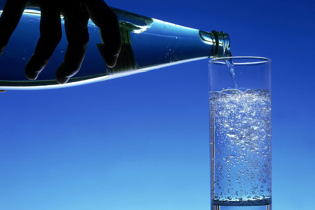 Pouring carbonated water from a bottle to a glass on a blue background