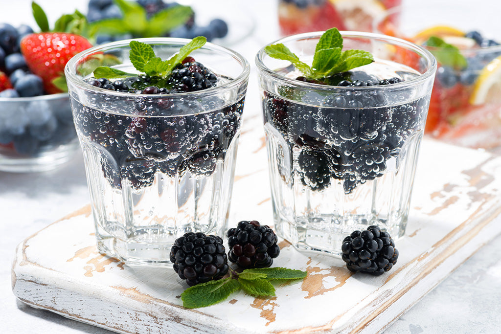 Two glasses of carbonated water with blackberries floating inside them