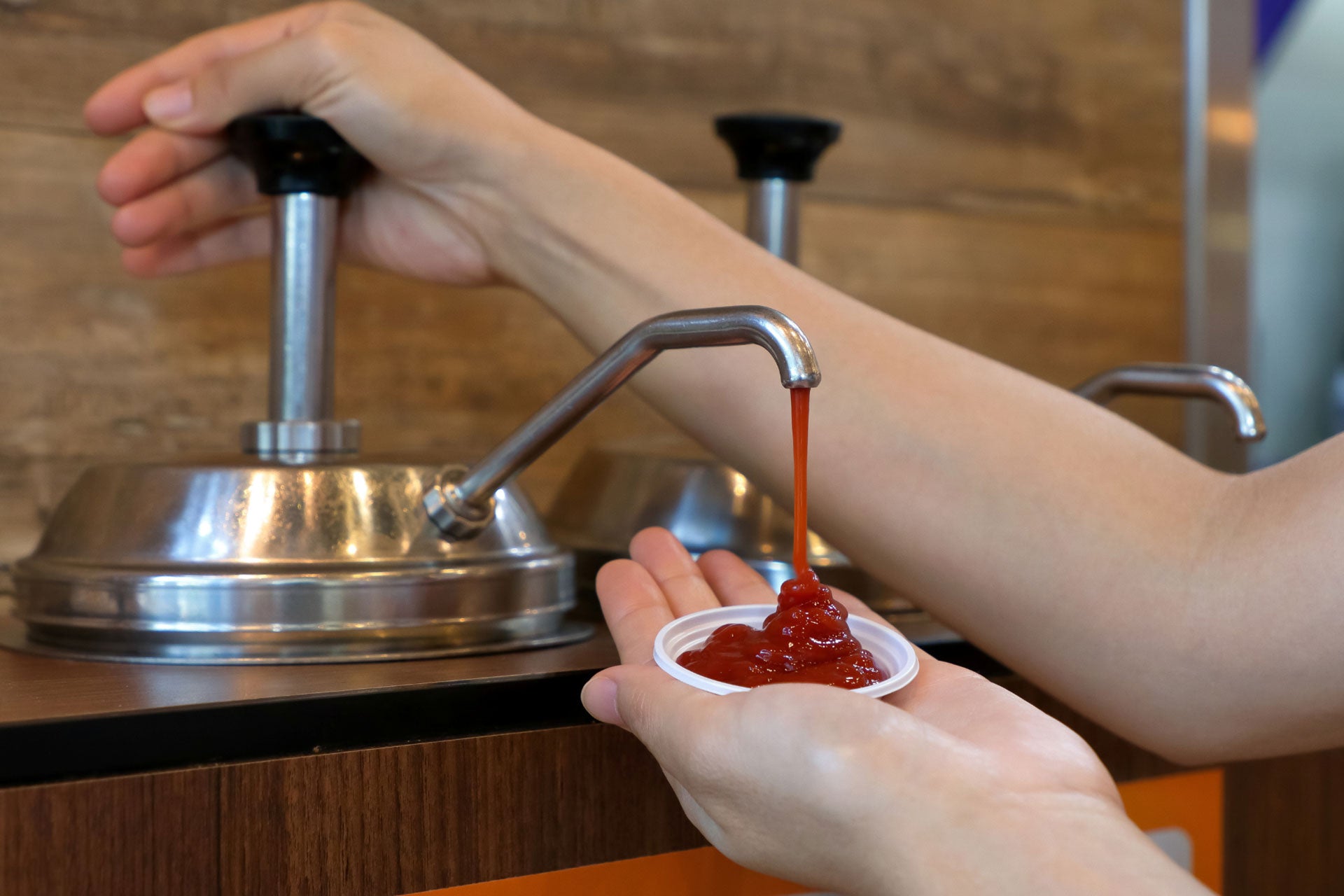 A customer dispenses ketchup from a self-serve pump into a ramekin