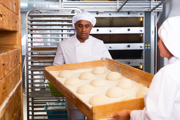 two bakers move loaves of bread to a proofing cabinet to rise