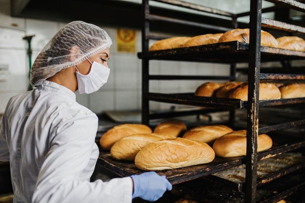 A baker inserts a pan of fresh bread into a sheet pan rack to cool