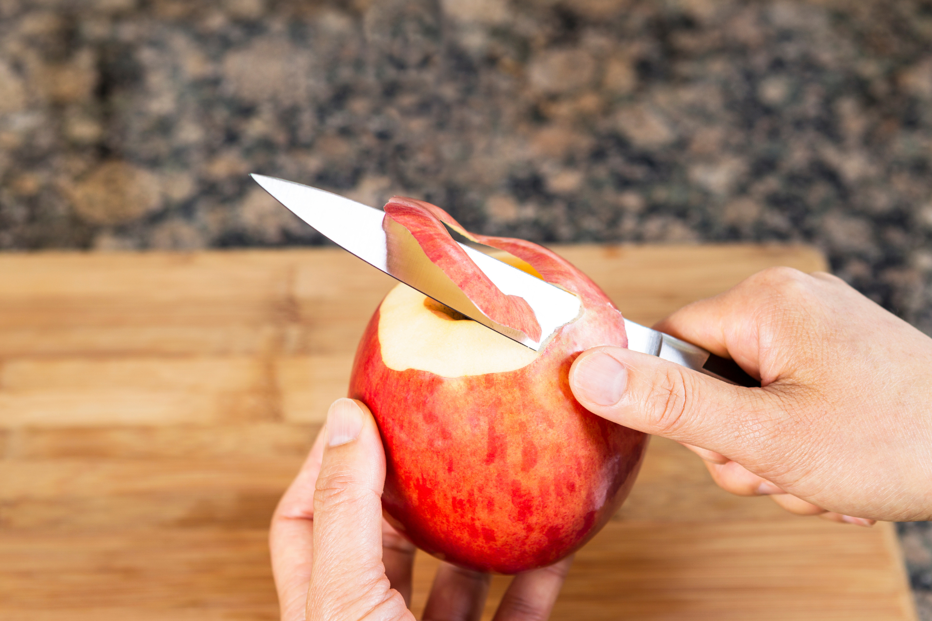 Close-up of a person’s hands using a peeling knife to peel an apple
