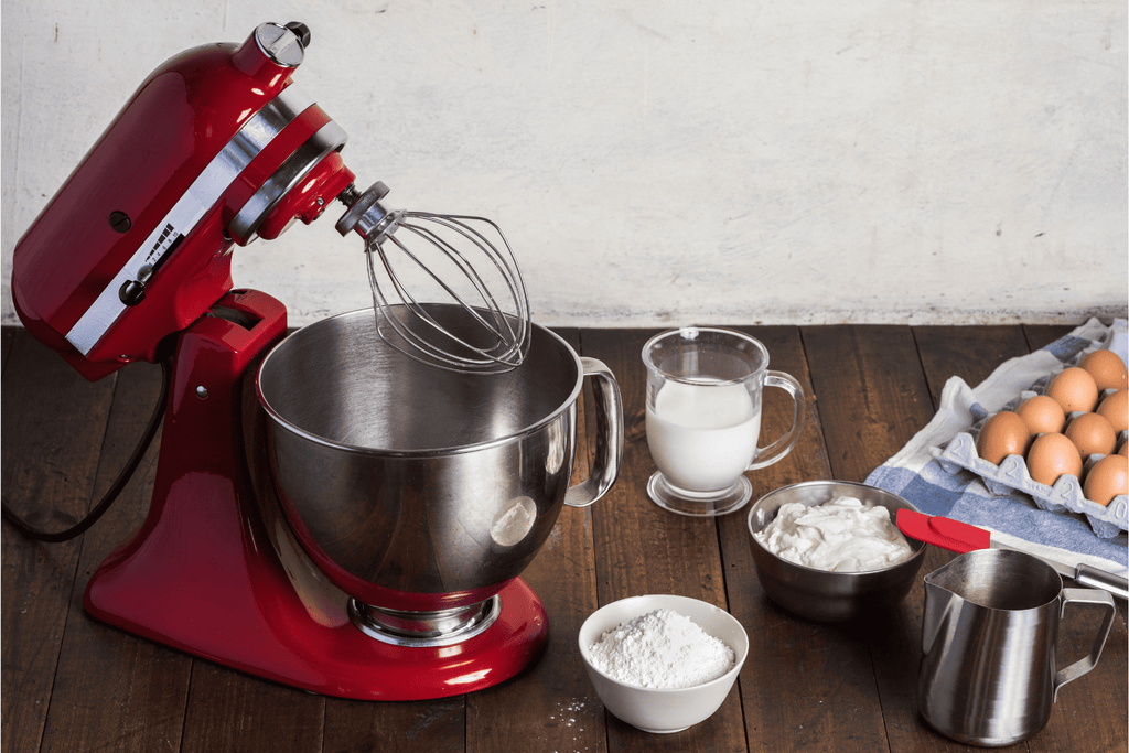A red KitchenAid mixer on a table with baking ingredients