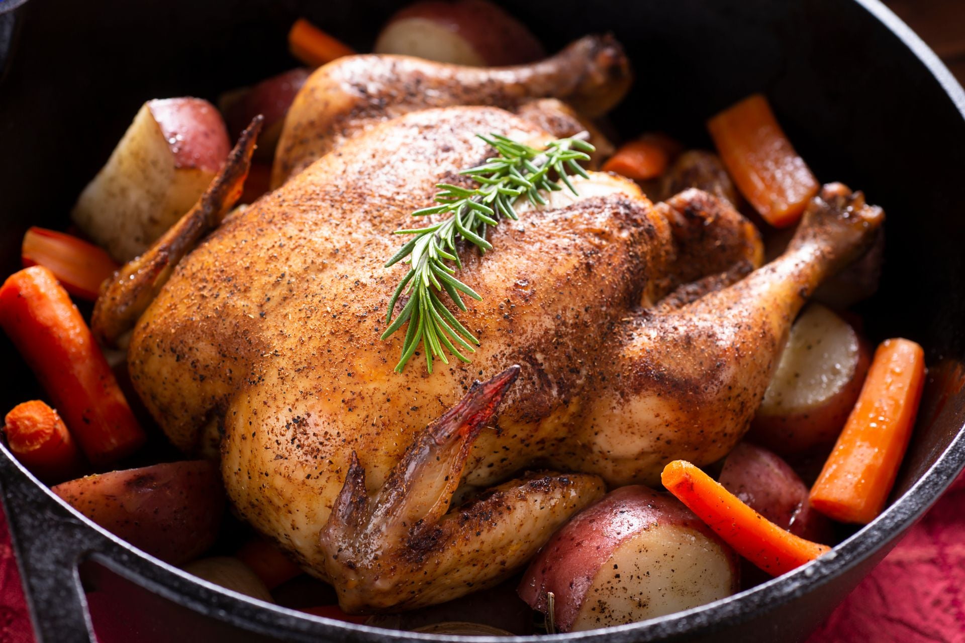 A roasted chicken, carrots, and potatoes cooked in a Dutch oven