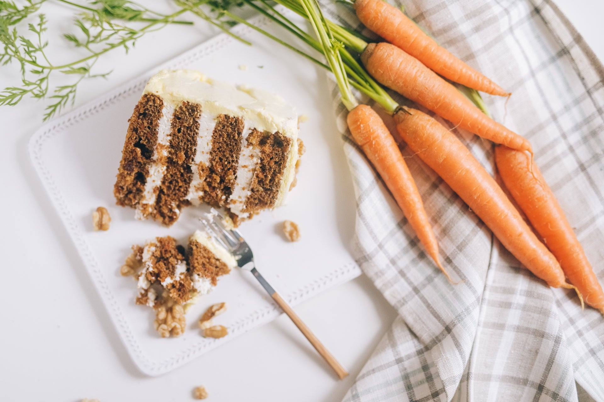 A slice of carrot cake placed beside a bundle of carrots