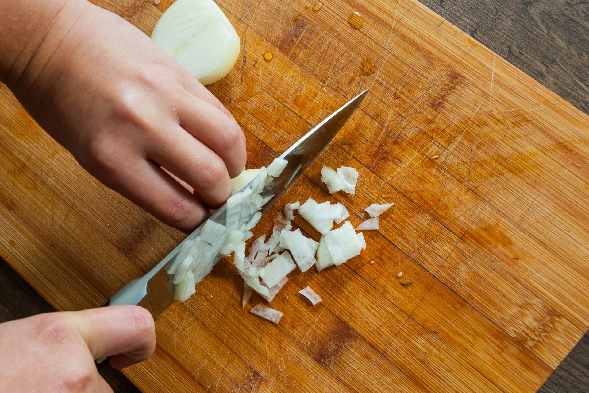 A person chopping onions on a wooden block using a stainless steel knife