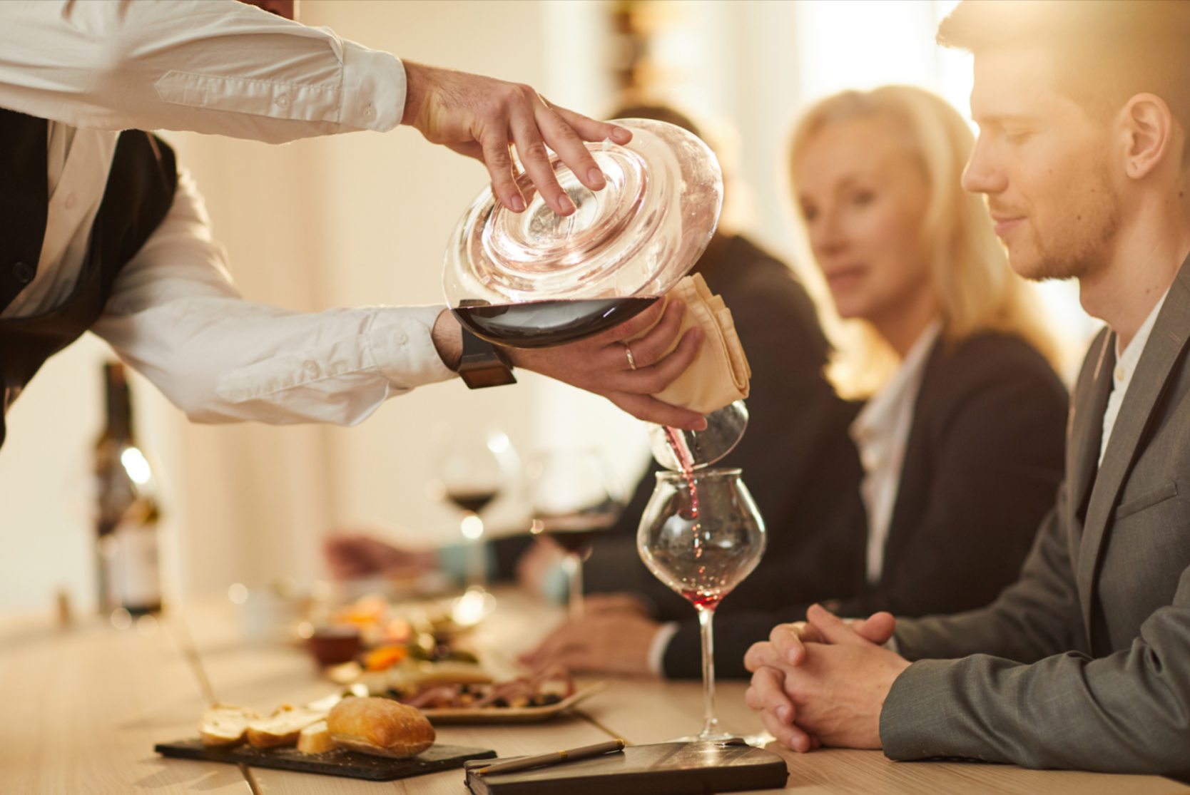 A server pouring wine from a decanter into a red wine glass