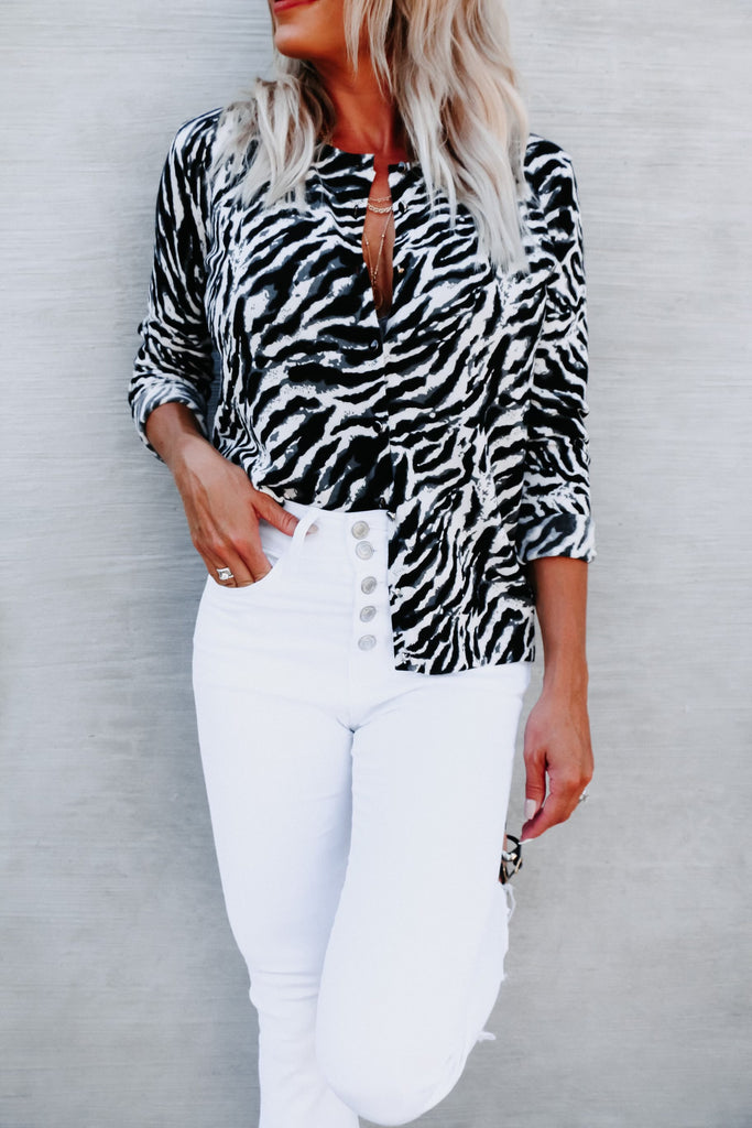 blonde woman wearing an animal print blouse with white jeans