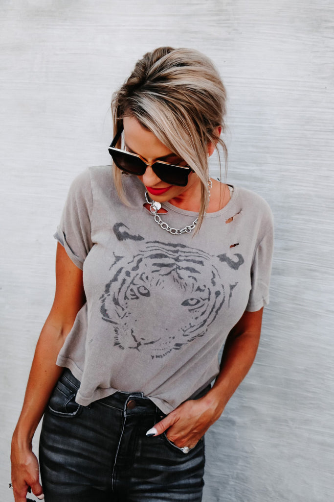 blonde woman with hair pulled back looking down wearing a gray distressed t-shirt with a lion on it and jeans