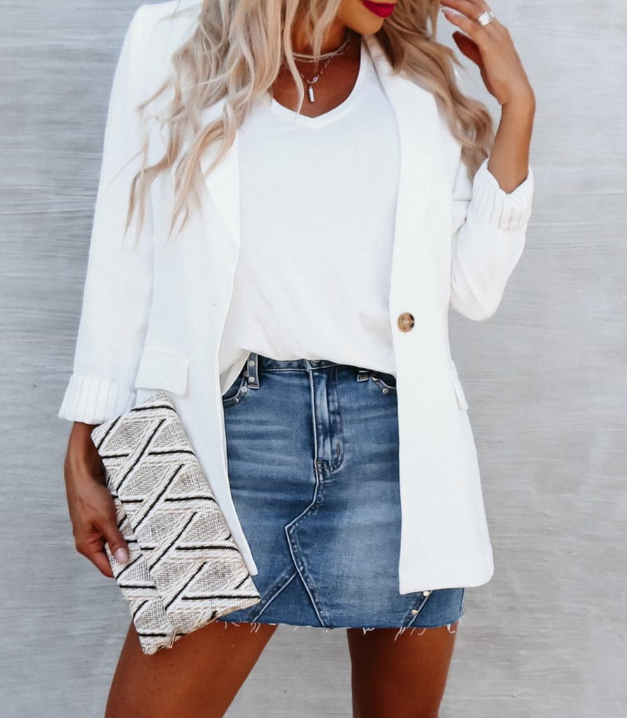 mid-section shot of blonde woman wearing a white cardigan over a t-shirt and a jean skirt, holding a white diamond textured clutch