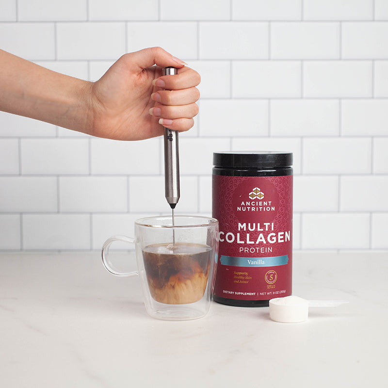 person using hand held frother in a clear glass mug of coffee