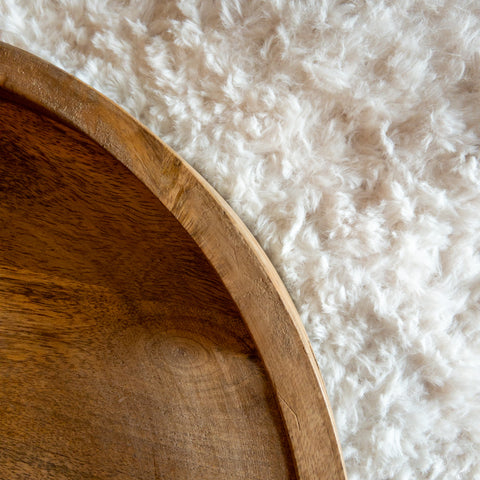 Close up of a brown round wooden tray resting on a crocheted cream-colored faux fur background