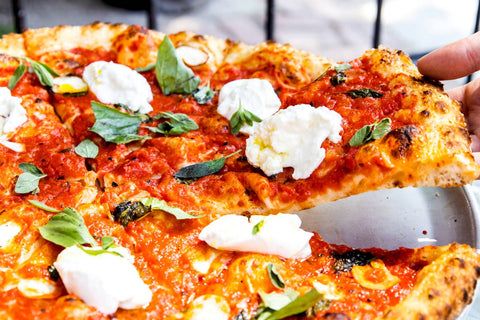 A close up of a person grabbing a slice from a Pizzeria Badiali margarita pizza.