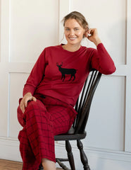 A person is seated on a chair wearing red pajamas with a black deer silhouette on the top.