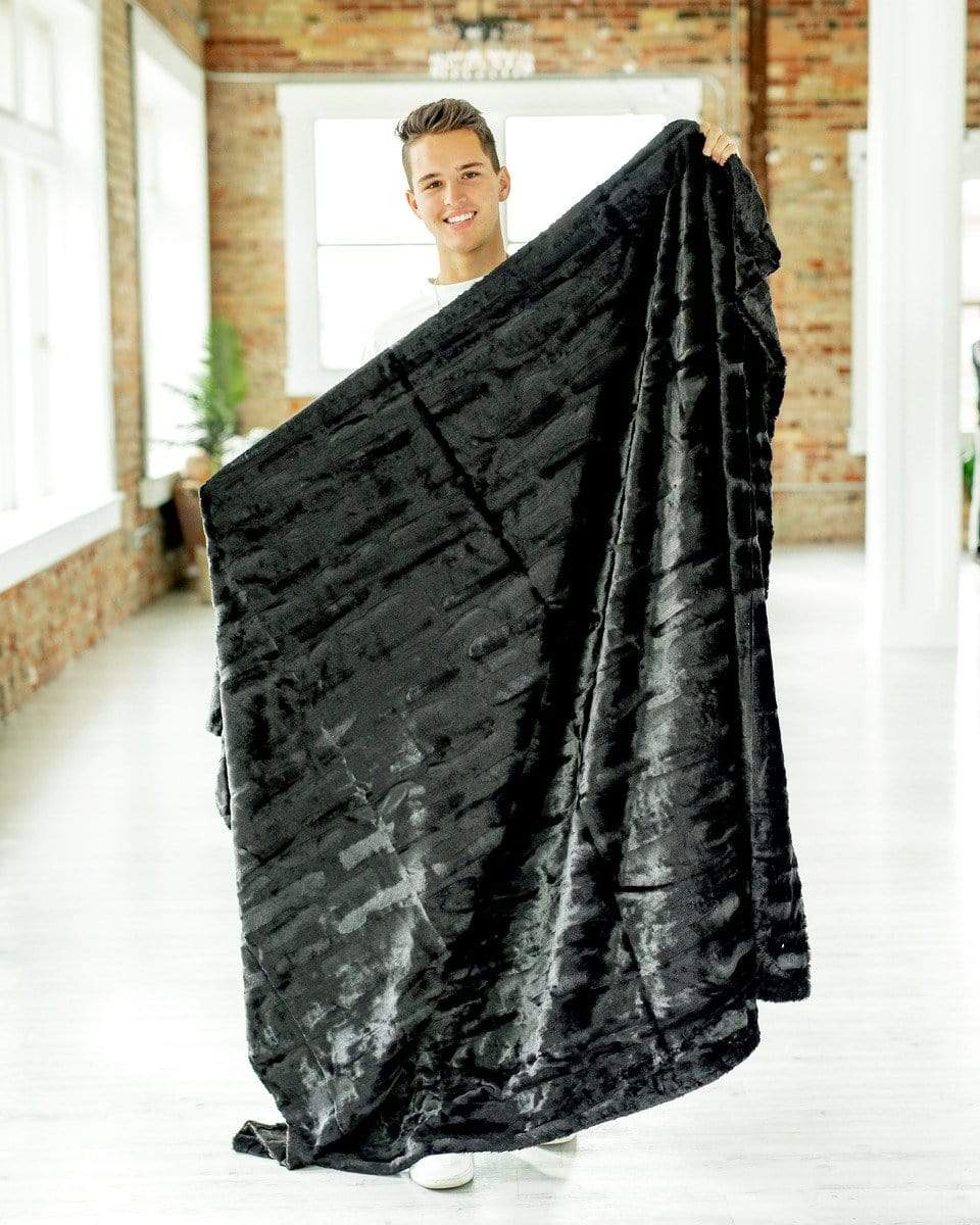 Young man holding a silky black plush blanket by Minky Couture.  Zoom - 2