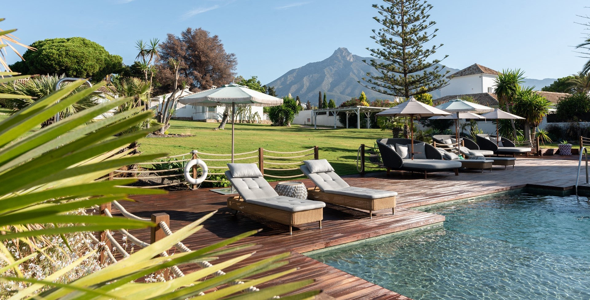 Sunbeds under white parasol and many daybeds with parasols by the poolside at the Boho Club, Marbella with nature around