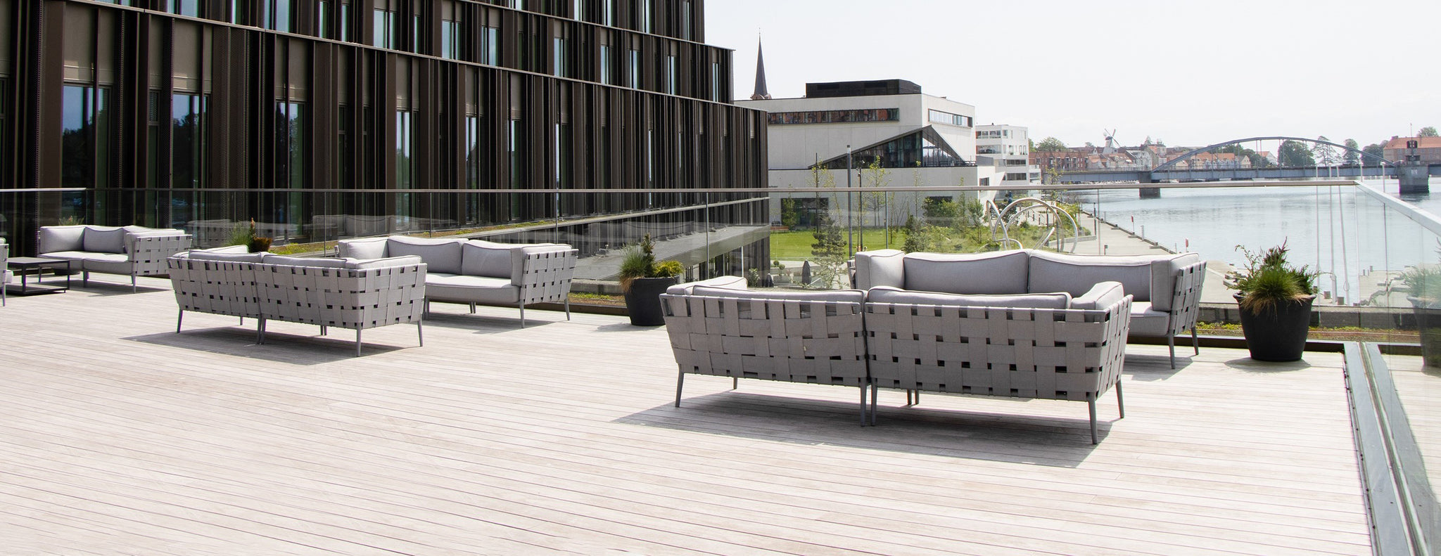 Five light grey lounge sofa groups from Cane-line Conic series on a terrace at Alsik Hotel with view over Alssund
